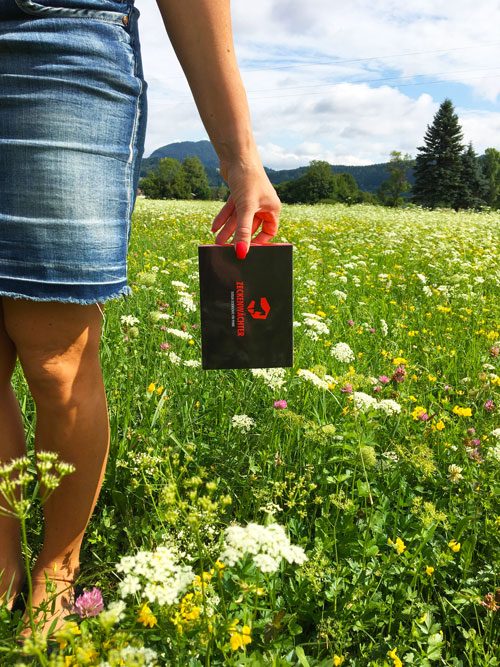 Sommerwiese, in der Hand die schwarz-rote Zeckenwächter-Verpackung